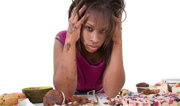 Junge Frau, die vor Kuchen und Süßigkeiten sitzt und verzweifelt ist