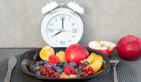 Teller mit frischem Obst vor analogen Uhr, die acht uhr anzeigt
